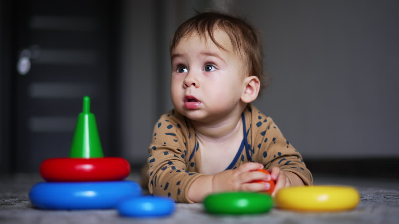 Adorable baby boy lies on the floor looking up with surprise. Child touches the parts of toy pyramid lying unfold in front of him.