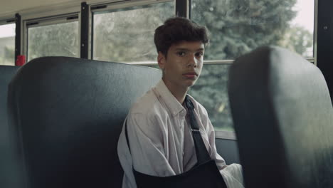 indian pupil looking camera sadly close up. teen boy sitting in school bus.