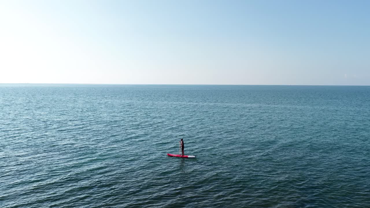 Man paddle boarding on calm ocean under blue sky