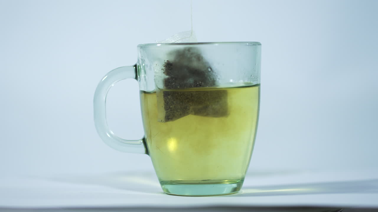 un primer plano de una taza de vidrio transparente con agua caliente, con una bolsa de té que se está empapando.