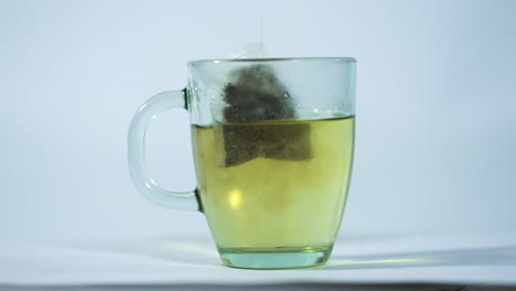 close-up shot of a transparent glass mug with hot water, featuring a tea bag being steeped.