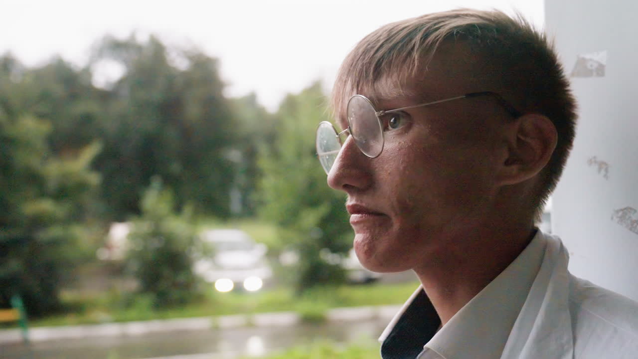 Close side view of botany student in white coat drinking unusual green beverage from bottle during outdoor break, showing refreshing moment of hydration in calm urban natural environment