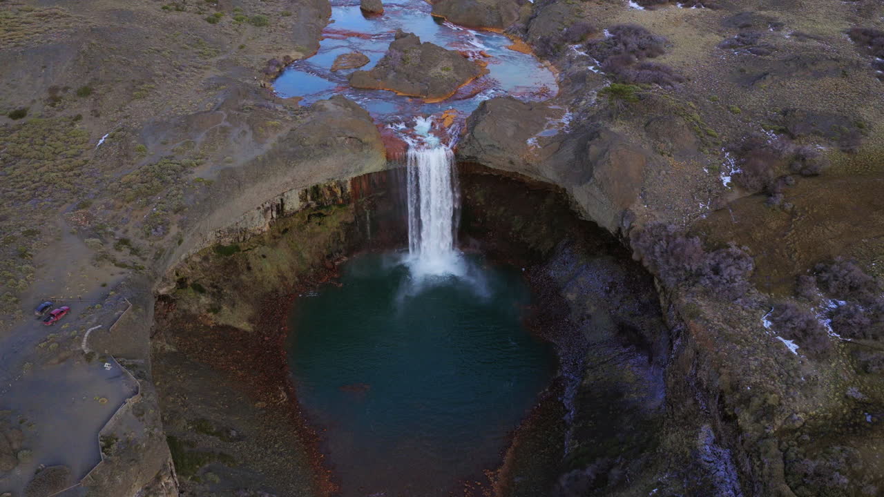 Top-down aerial view of Salto del Agrio waterfall cascading into a turquoise pool surrounded by volcanic cliffs in Caviahue
