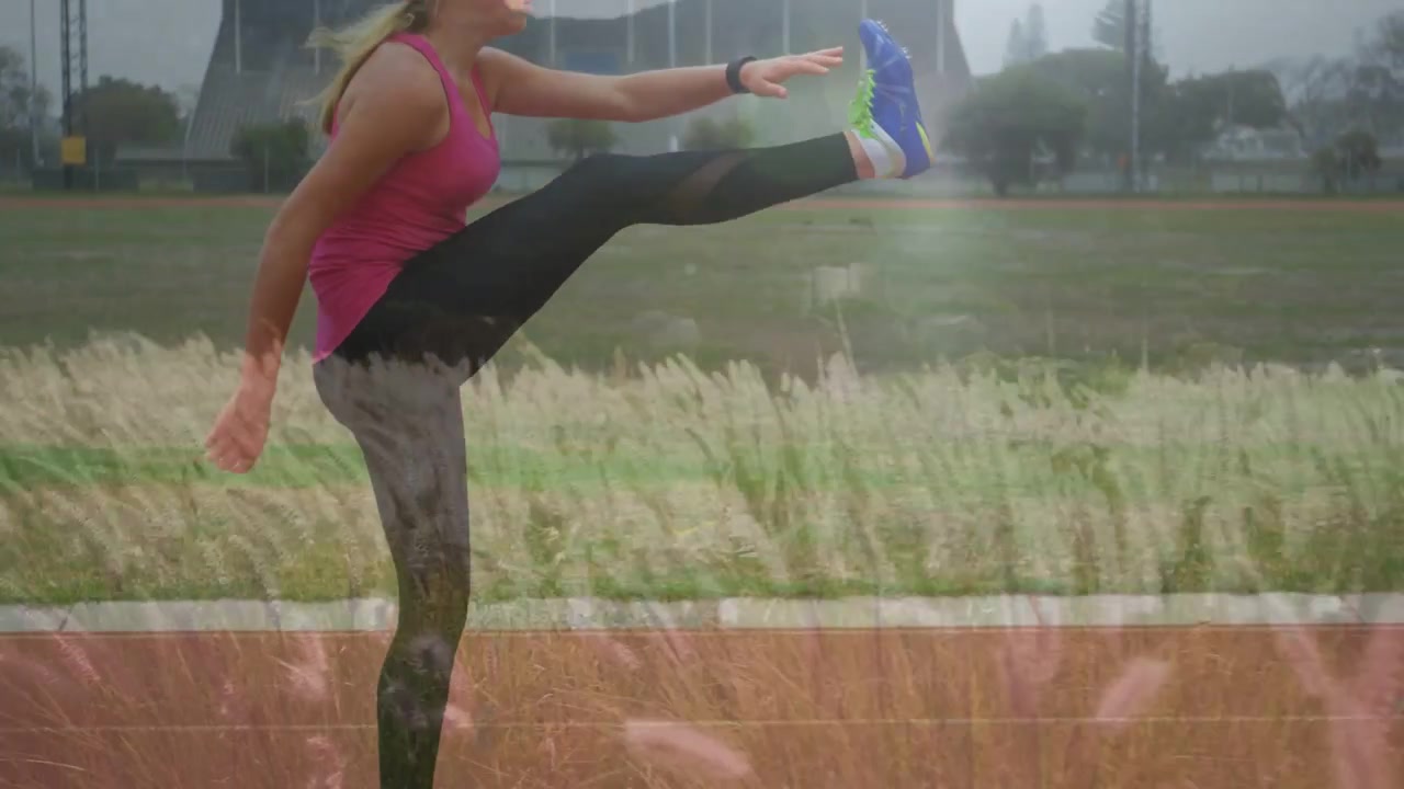 Girl warming up on track, swinging leg, balancing with grass overlaying her for training
