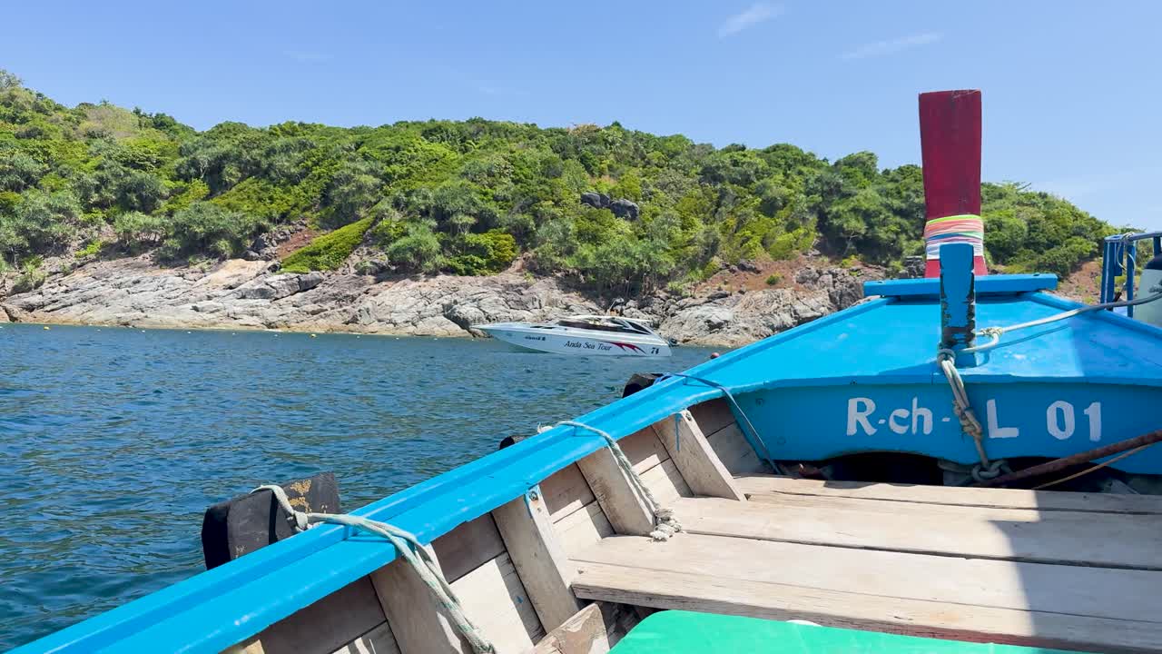 A vibrant boat glides through clear waters near Phuket, Thailand, under bright sunlight with lush greenery in the background