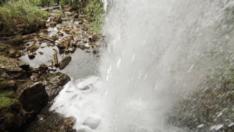 Cámara-Que-Muestra-Y-Se-Mueve-Detrás-De-Una-Cascada,-A-La-Luz-Del-Día,-En-Una-Región-Montañosa