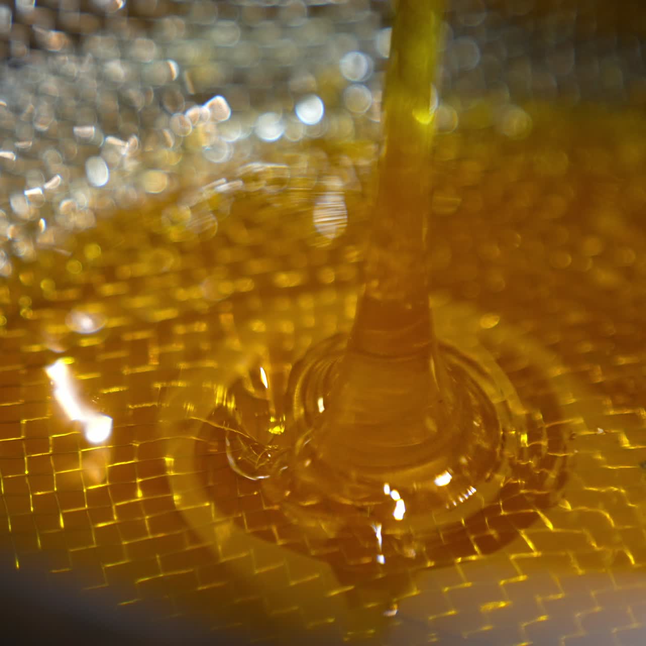 Thick yellow honey flowing on the metal sieve. Freshly gathered organic product at the rural apiary. Close up