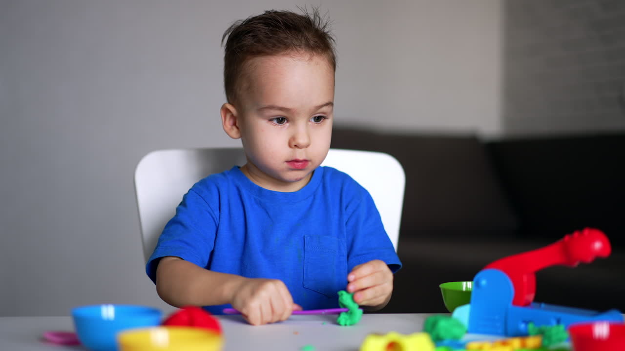 Bambino caucasico dagli occhi scuri con una maglietta blu taglia la plastilina con un bastoncino. Il bambino finisce di modellare e si alza
