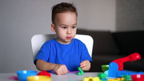 dark-eyed caucasian baby in blue t-shirt cuts the plasticine with a stick. kid finishes sculpturing and stands up.