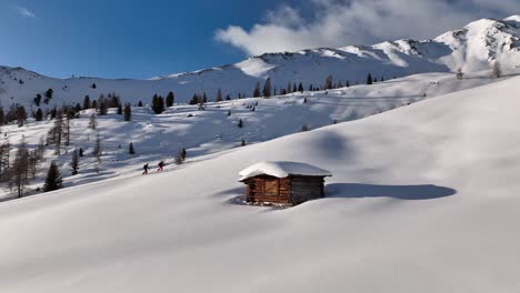 two alpine ski tourers passing an old hut on the ascent