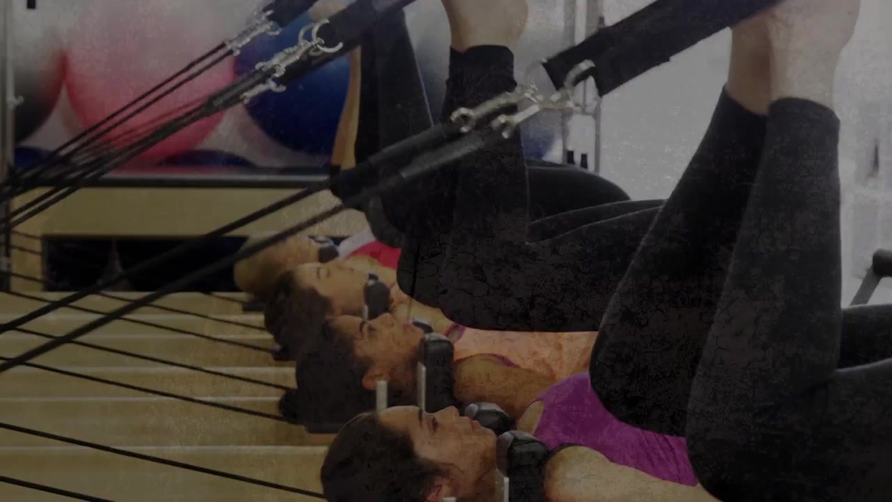 Vertical video: Pulling back showing five women bridging on reformers in studio class in tanks