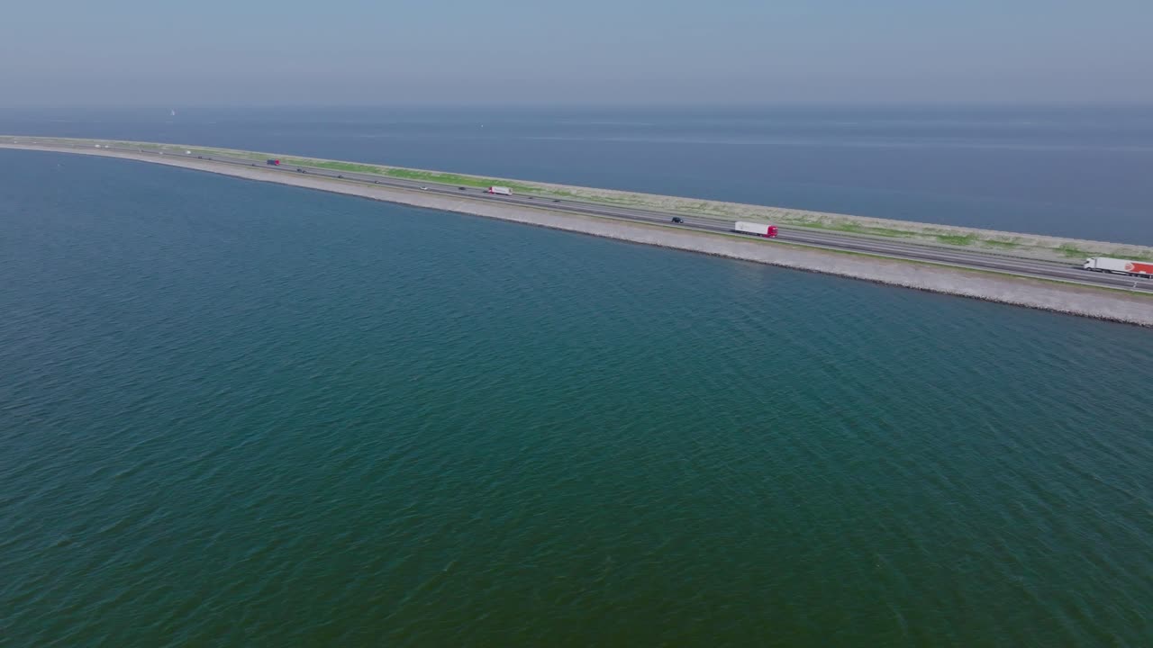 Drone pan left following the Afsluitdijk dam and its straight road dividing two vast bodies of water under clear sky