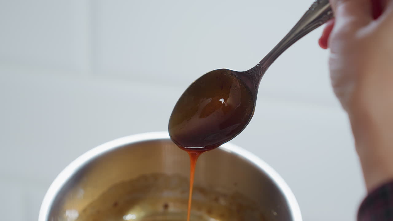 Close-up of golden palm oil being poured from spoon into pot, creating a rich, glossy texture, oil flows smoothly, reflecting warm light, as the pot sits on modern kitchen counter