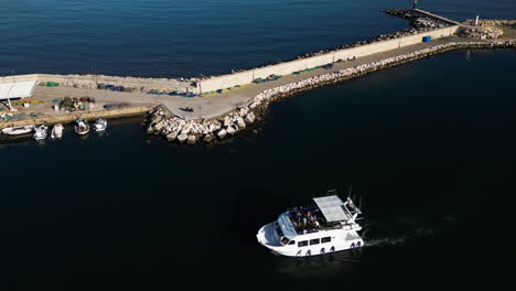 White-yacht-with-people-partying-entering-port,-aerial-drone-view