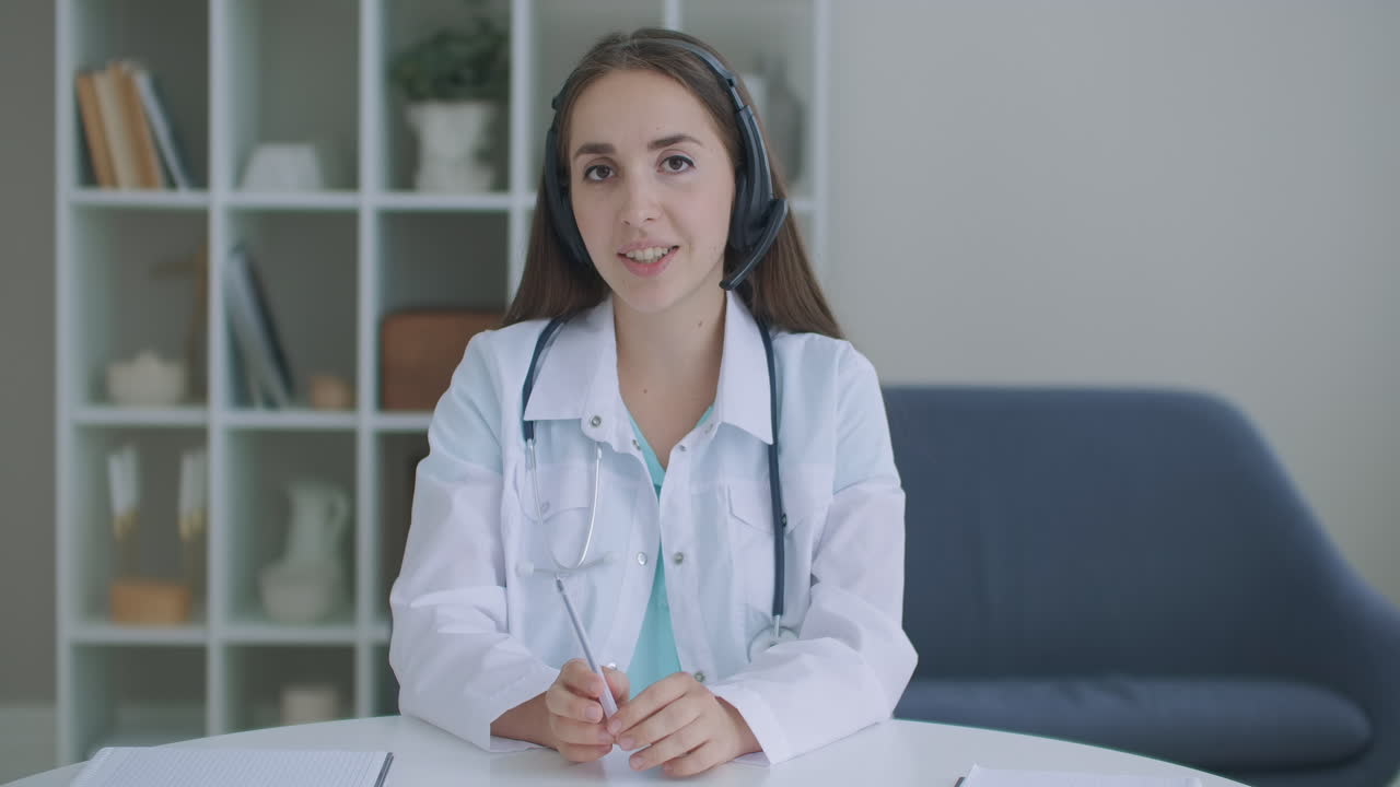 doctora joven sonriente vestida con uniforme blanco estetoscopio consultando paciente en línea a través de videollamada mirando a la cámara hablando cámara hacer video chat a distancia telemedicina y concepto de e-salud cámara web