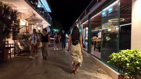 rear view of a tourist girl walking down the narrow pathway in schisma eloundas during nighttime in greece.