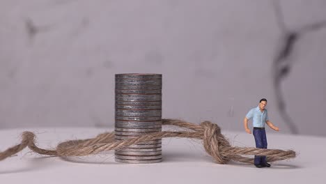 a miniature man woven with piles of coins and ropes.