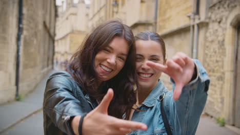 same sex female couple pose for photo making shape of frame with hands as they visit city together