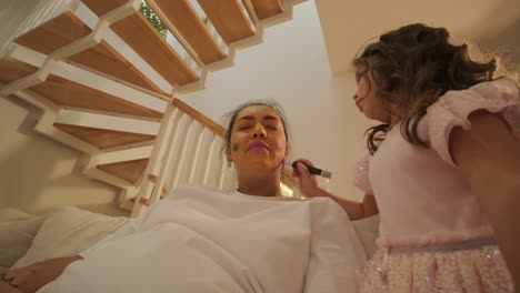 niña pequeña aplicando maquillaje a su madre embarazada en casa