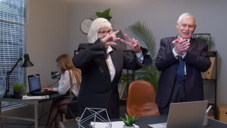 two joyful collegues in formal suits dancing victory dance, celebrating success of business project