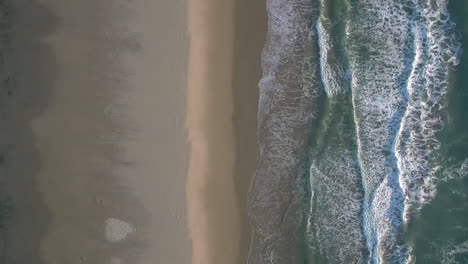 aerial drone shot looking down, symmetrically aligned with beach shore and sea waves crashing