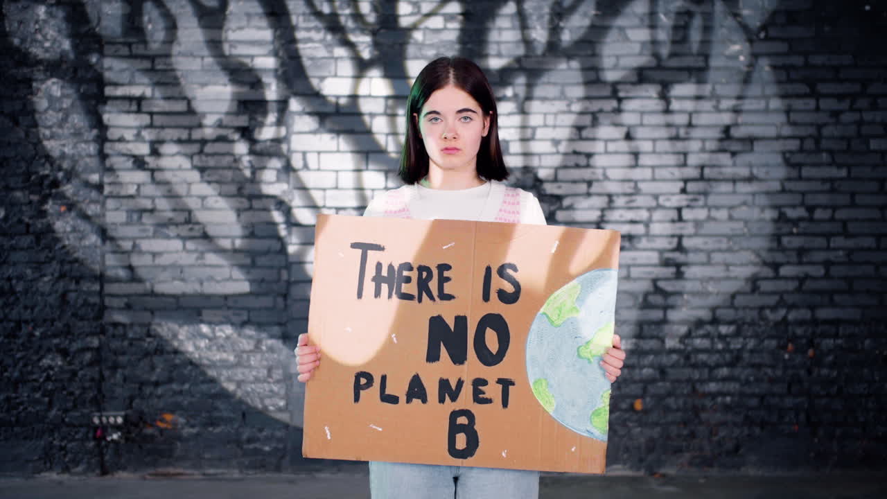 серьезный молодой экологический активист держит картонку с надписью "нет планете b" и смотрит в камеру".