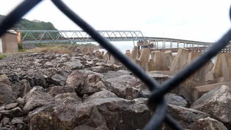 coastal marine engineering defence shaped blocks and pier viewed through chain link fence close up pull back