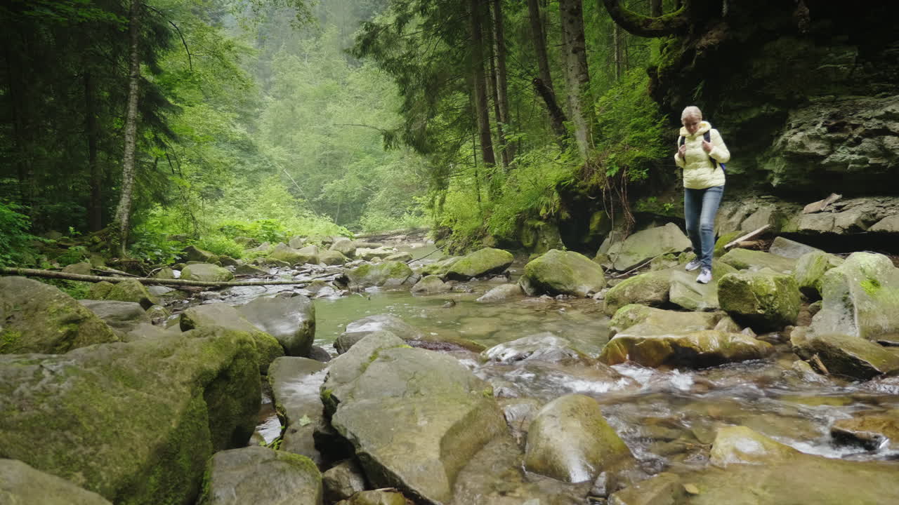 una turista con mochila cruza un río de montaña en las aventuras del bosque y de manera activa