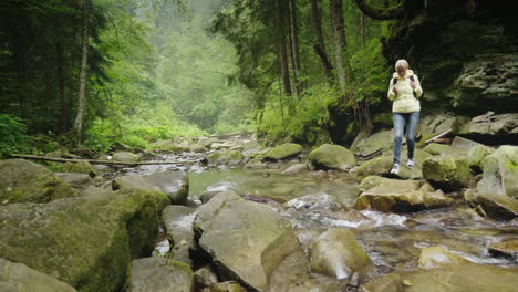 a female tourist with a backpack crosses a mountain river in the forest adventures and an active way