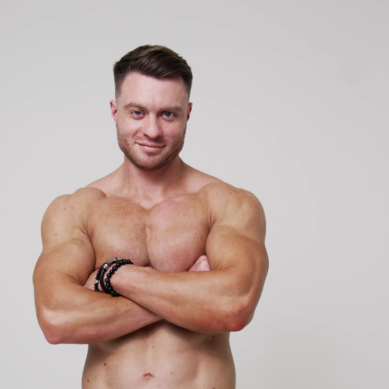 Uomo caucasico in piedi di spalle alla camera si gira verso la camera. Atleta a torso nudo incrocia le mani sul petto guardando la camera. Sfondo bianco
