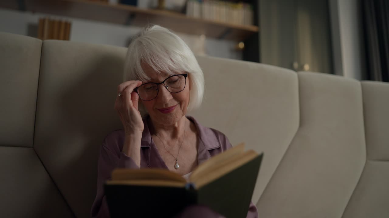 Elderly woman reading a book on the couch