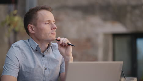 close-up portrait of ponder young man in office. designer plans his work and holding a pencil in his hand. shooting is slow motion from below. thoughtful serious man sit with laptop thinking solution