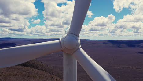 aerial moving away from rotating wind turbine on sunny day with white clouds