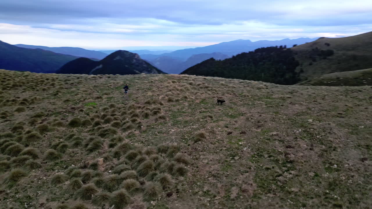 disparo de dron de una mujer corriendo con su perro en una cordillera mientras el dron da vueltas a su alrededor