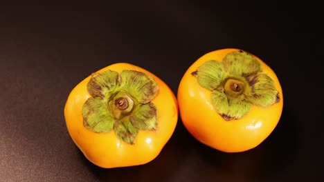 two persimmons rotating on a dark background