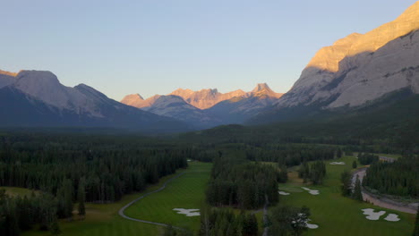 drone aerial view of green golf course with alpine glow in the rocky mountains of banff and kananaskis of alberta, canada at sunrise