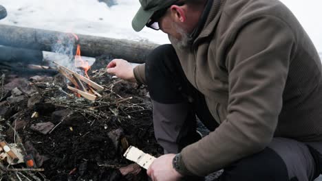 man putting small twigs on campfire, slow motion