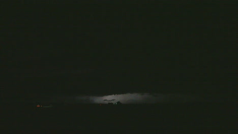 lightning pulses flash in the night sky as cars drive along a road