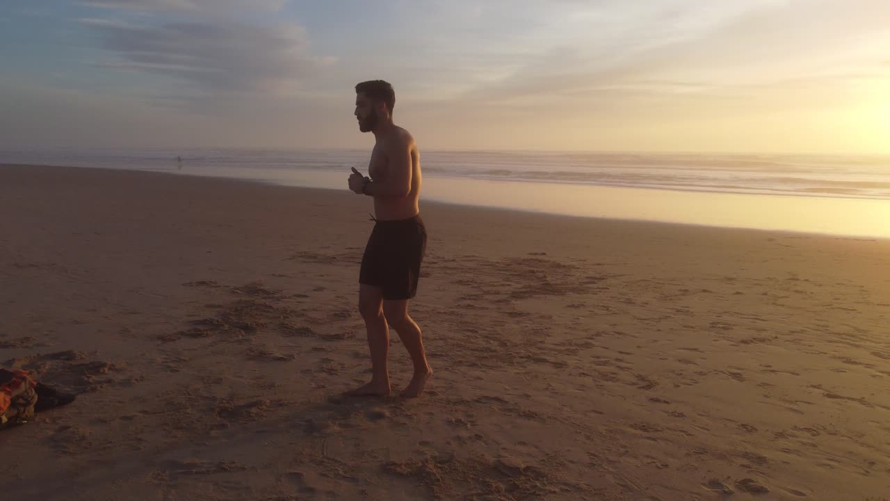 A dynamic shot of a man practicing martial arts on a beach, with an amazing background sunset and ending with a powerful fly-away shot.