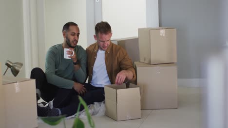 multi ethnic male same sex couple drinking coffee and packing to move house