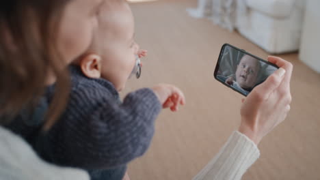 Mamá-Y-Bebé-Usando-Un-Teléfono-Inteligente-Teniendo-Video-Chat-Con-Un-Hermano-Pequeño-Saludando-A-Una-Madre-Feliz-Disfrutando-De-Una-Reunión-Familiar-En-La-Pantalla-Del-Teléfono-Móvil