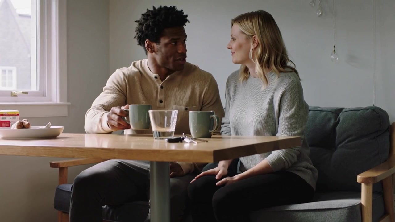 Settling couple in sweaters reaching table at home nook, sharing morning, man sipping mug with keys
