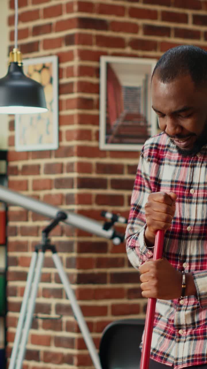 Vertical video: Modern happy boyfriend having fun with music while he uses mop to wash floors