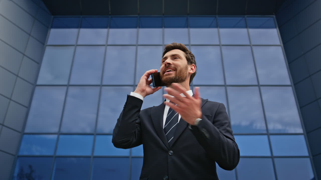 Cheerful manager calling phone standing near glassy urban building closeup