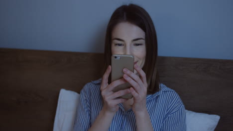 close-up view of the charming caucasian woman with dark hair lying in the bed, chatting on the smartphone late at night