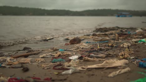 still shot of garbage and used plastic in the sand on a riverbank