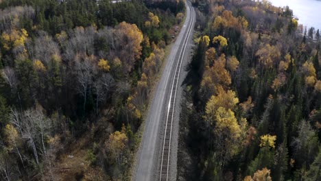 Aerial-dolly-left-over-train-tracks-running-through-idyllic-autumn-boreal-forest-in-the-Canadian-shield