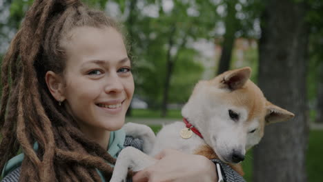 woman with dreadlocks holding her shiba inu dog in a park