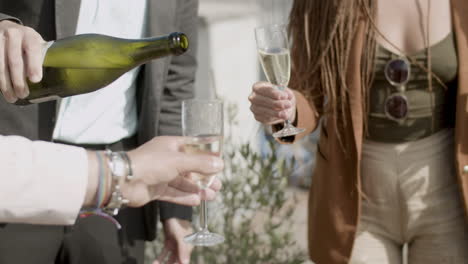 medium shot of man pouring sparkling wine into glasses at party