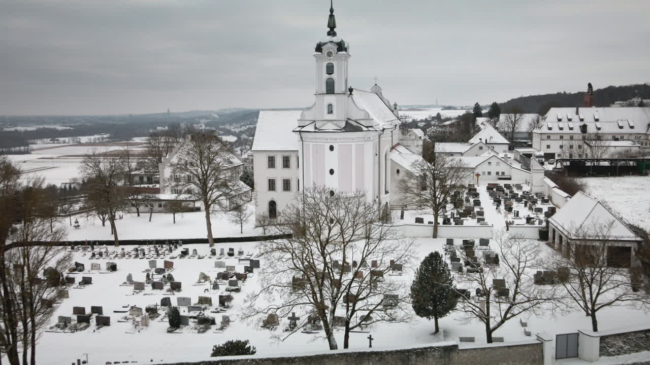 Un drone 4K si allontana allargando l'inquadratura da una chiesa innevata e un cimitero fino a un villaggio. Il fluido movimento all'indietro offre una serena inquadratura invernale, ideale per promozioni, documentari e immagini turistiche.